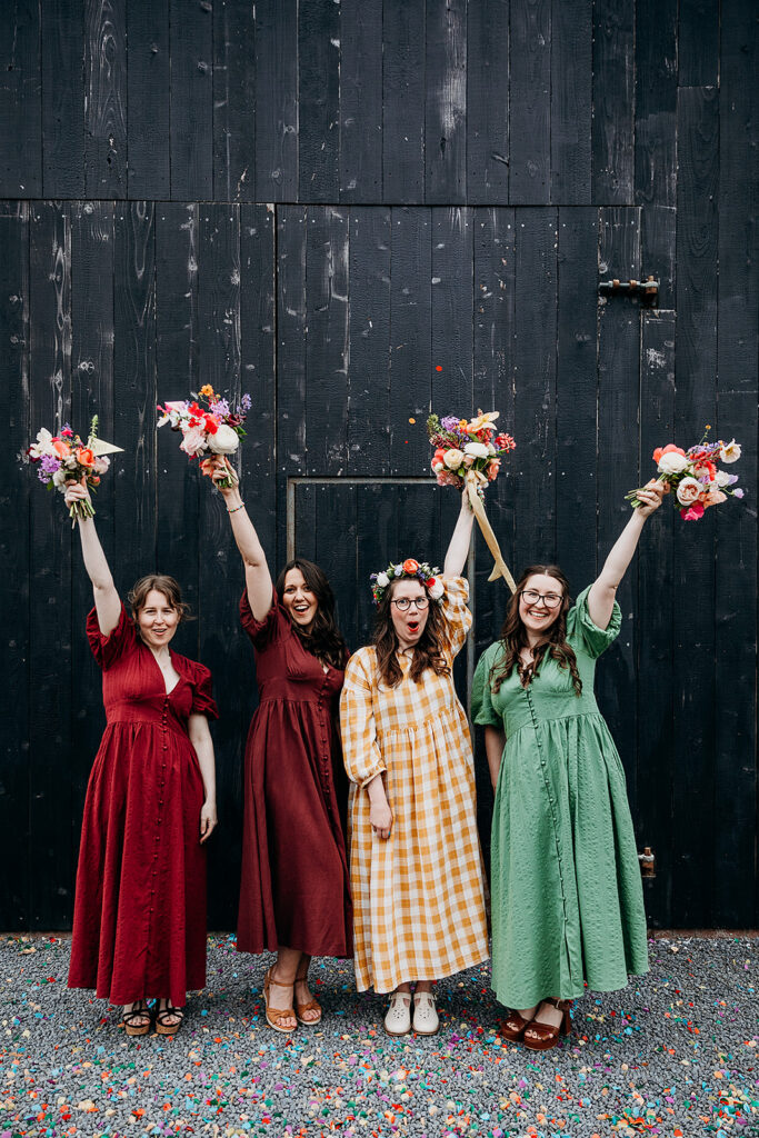 Bride and bridesmaids with flowers in the air at The Giraffe Shed