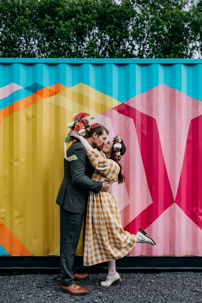 Bride and Groom kissing in front of colourful shipping container at The Giraffe Shed