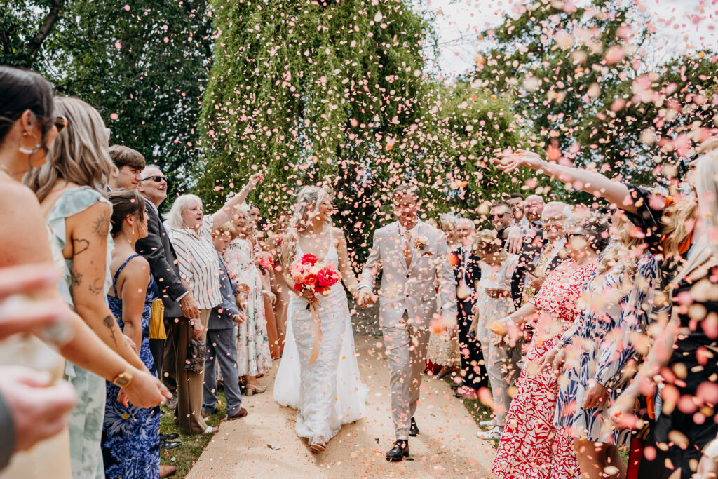 Bride and groom walking through pink confetti in garden wedding ceremony