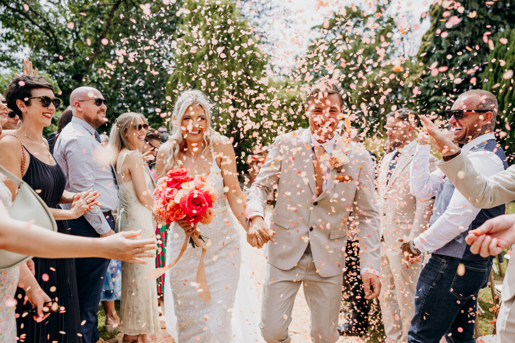 Bride and groom walking through pink confetti in garden wedding ceremony