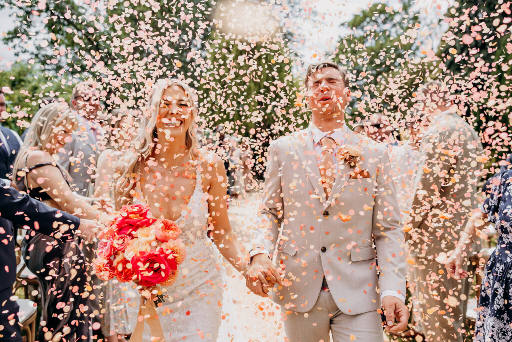 Bride and groom walking through pink confetti in garden wedding ceremony