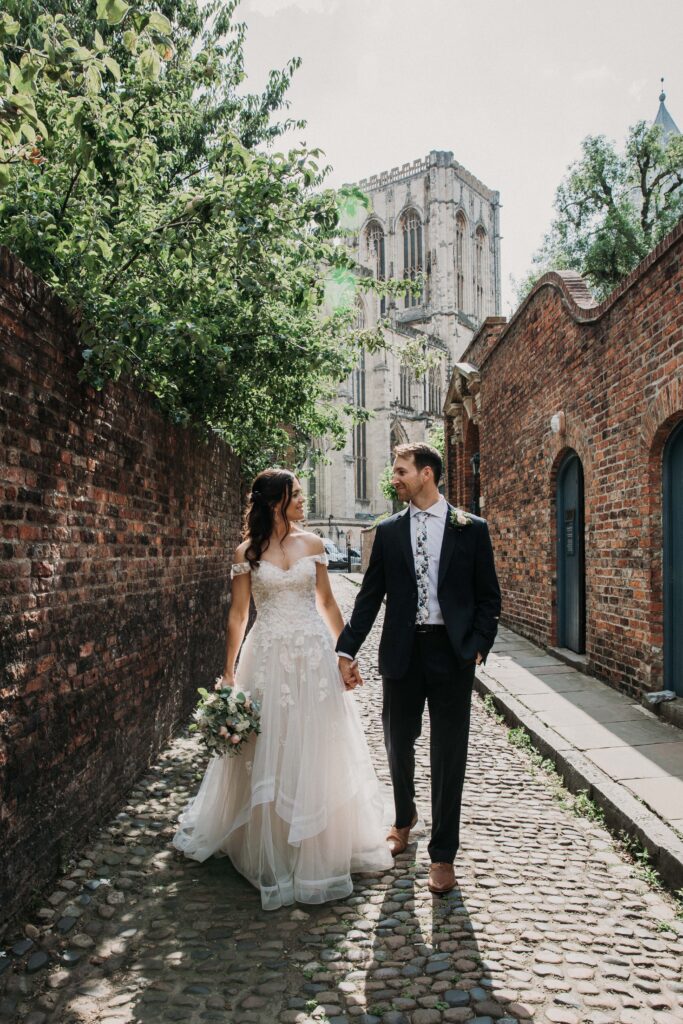 Bride and Groom walking down cobbled street with York Minster in the background