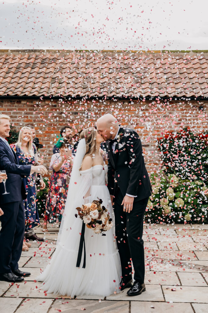 Bride and Groom kiss in confetti at Thirsk Lodge Barn