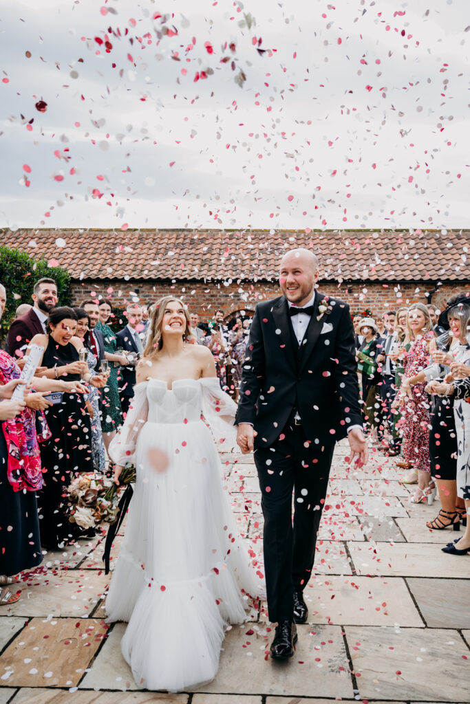 Bride and Groom walk through confetti at Thirsk Lodge Barn