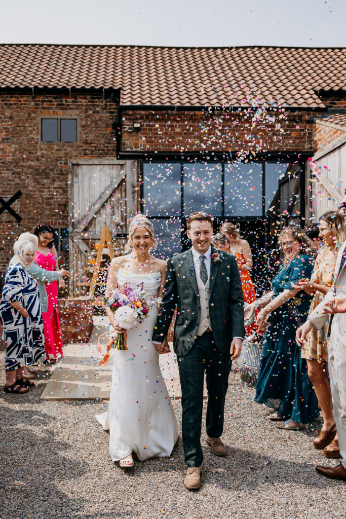 Bride and Groom walk through confetti at Woolas Barn