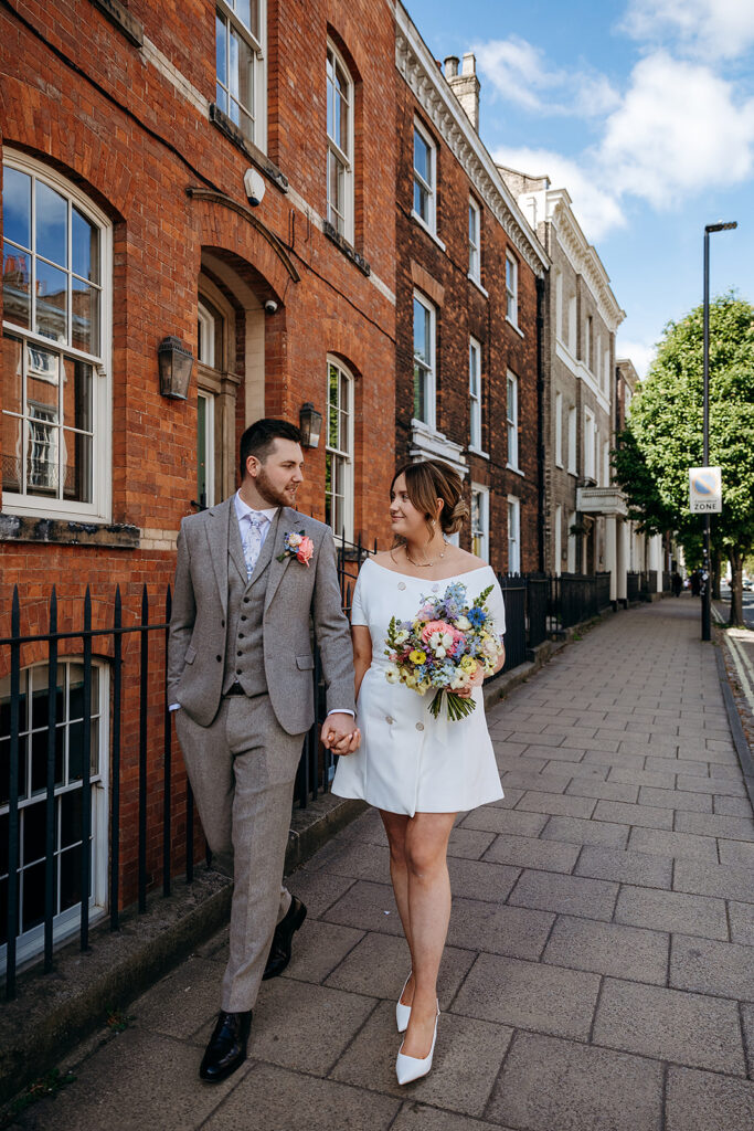 Bride and groom walking through street in York. bride has colourful flowers and short wedding dress in York